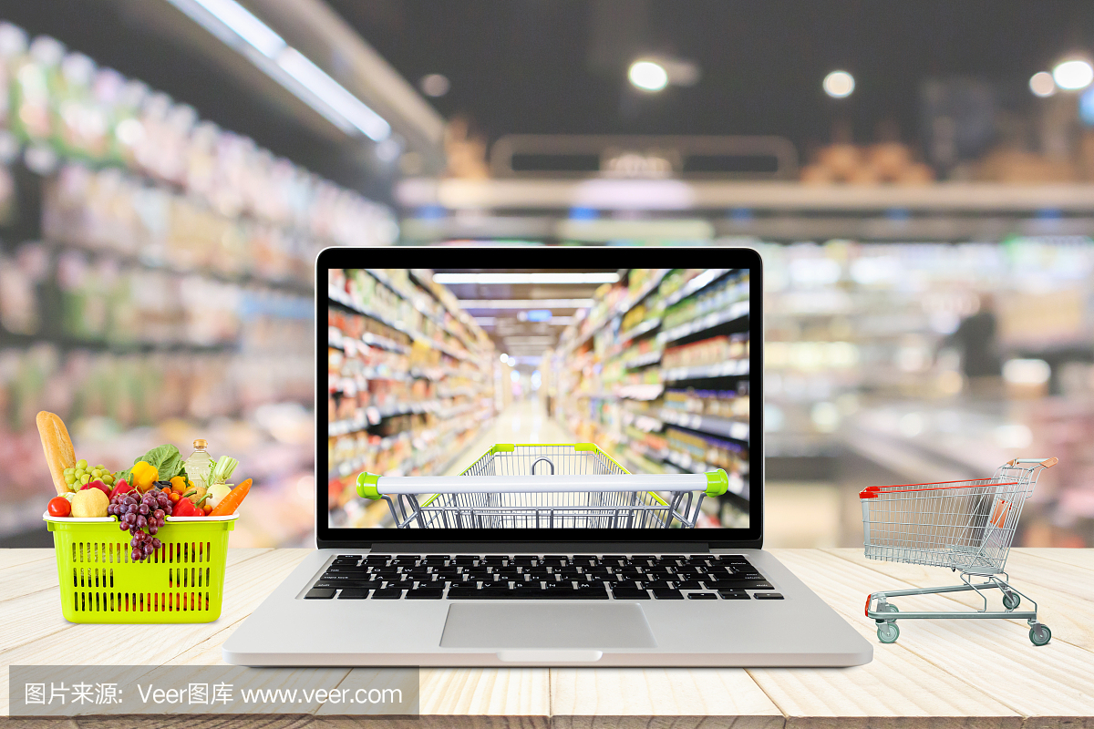 超市过道模糊的背景与笔记本电脑和购物车木桌子上的网上杂货概念